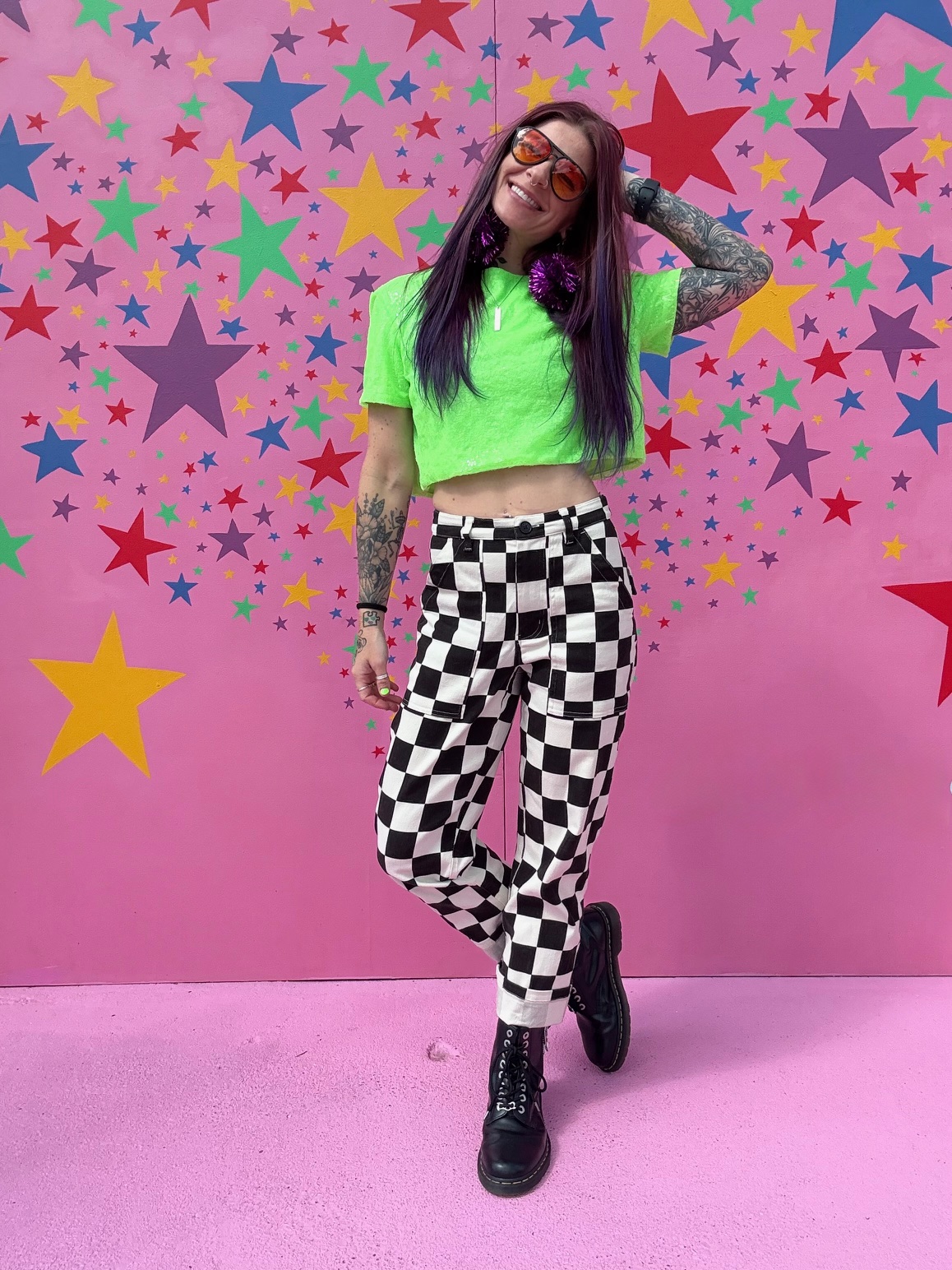 Zoomz, content and social lead at Broccoli Media, posing in a neon green top and checkered pants against a pink star mural